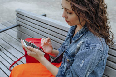 Junge Frau mit Smartphone auf einer Bank sitzend - OGF00469