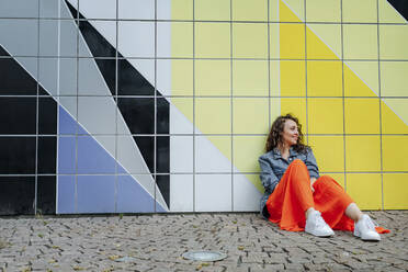 Junge Frau sitzt in der Stadt auf dem Boden und lehnt sich an eine gekachelte Wand - OGF00478