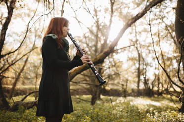 Junge Frau übt Klarinette spielen, während sie im Herbst im Wald steht - MRRF00268