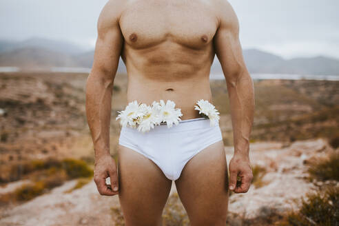 Man wearing underwear with flowers in field during sunset - MIMFF00170