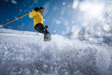 Ganzkörper junger Mann in gelber Kleidung und Sonnenbrille beim Skifahren auf einem verschneiten Berghang an einem sonnigen Wintertag am Urlaubsort - ADSF10804