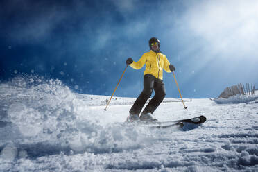 Ganzkörper junger Mann in gelber Kleidung und Sonnenbrille beim Skifahren auf einem verschneiten Berghang an einem sonnigen Wintertag am Urlaubsort - ADSF10805