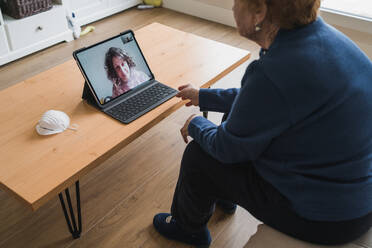 Seitenansicht von oben auf eine ältere Frau, die am Tisch sitzt und mit ihrer Tochter ein Online-Gespräch über einen Laptop führt, während sie während der Coronavirus-Pandemie zu Hause bleibt - ADSF10819