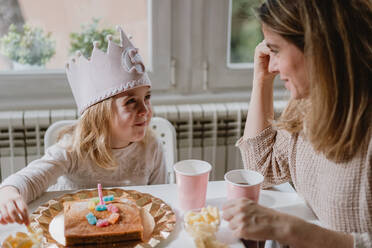 Positive Mutter in Freizeitkleidung sitzt am Holztisch und spricht mit Kindern, die zu Hause Geburtstag feiern - ADSF10855