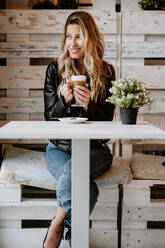 Long haired trendy beautiful blonde woman drinking from a glass of delicious foamy coffee while looking away - ADSF10874