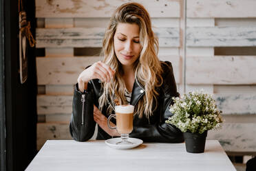 Long haired trendy beautiful blonde woman drinking from a glass of delicious foamy coffee with closed eyes - ADSF10875