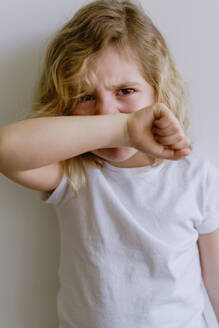 Naughty kid with wavy hair in casual clothing standing with folded arms and weeping looking at camera on white background - ADSF10923