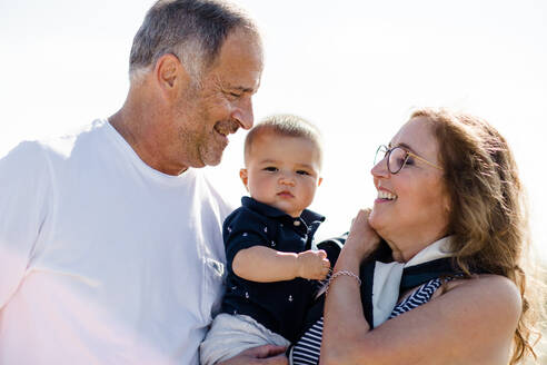 Großeltern lächelnd & halten Enkel am Strand - CAVF88088