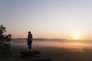 Silhouette eines Mädchens beim Wandern auf einem Berggipfel bei Sonnenaufgang - CAVF88110