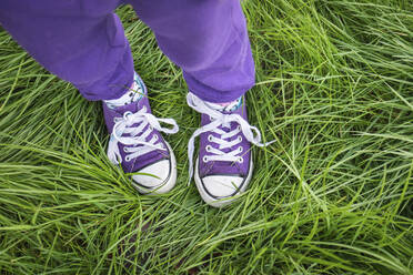 Girl wearing purple pants and shoes standing in long green grass - CAVF88138