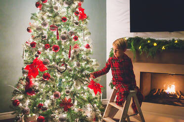 Junge hängt Weihnachtsschmuck an den Weihnachtsbaum bei Nacht - CAVF88166