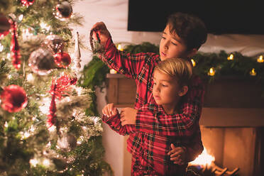 Zwei Brüder hängen nachts Ornamente an den Weihnachtsbaum - CAVF88167