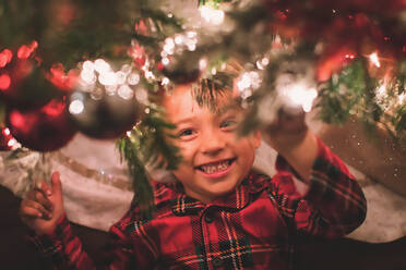 Junge hängt mit Blick auf die Kamera unter dem Weihnachtsbaum bei Nacht - CAVF88168