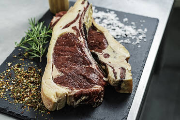 Raw steak, rosemary and salt on a serving board - CAVF88174