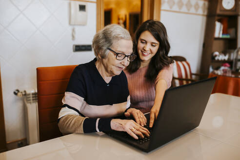 Enkelin bringt ihrer Großmutter etwas auf dem Laptop bei - CAVF88210