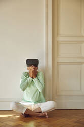 Ältere Frau benutzt einen Virtual-Reality-Simulator, während sie zu Hause auf dem Boden sitzt - MCF01031