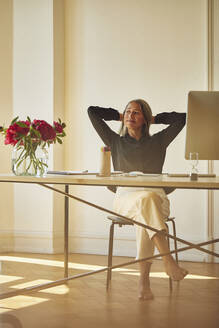 Businesswoman with hands behind head while sitting at home office - MCF01057