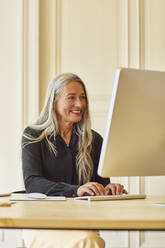 Lächelnde Geschäftsfrau, die zu Hause am Computer arbeitet - MCF01061