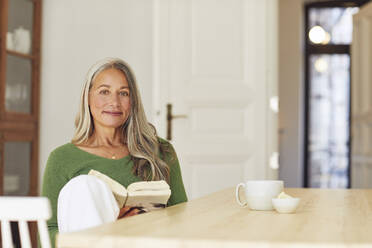 Frau mit Buch am Tisch sitzend zu Hause - MCF01065