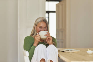 Smiling woman drinking coffee by table at home - MCF01072
