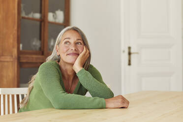 Smiling woman day dreaming while sitting by table at home - MCF01074