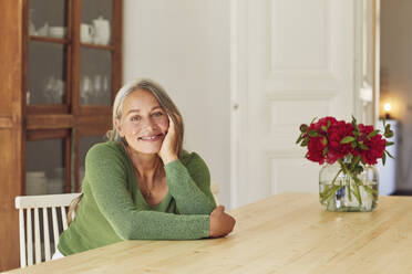 Smiling woman day dreaming by table at home - MCF01075