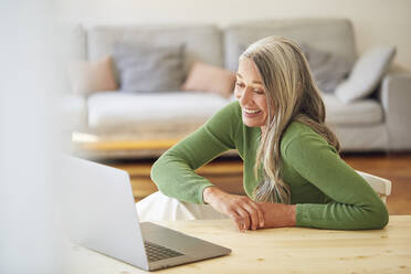 Happy businesswoman looking at laptop while sitting by table - MCF01080