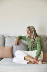 Smiling woman day dreaming while sitting on sofa at home - MCF01090