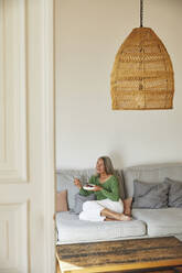 Woman eating breakfast while sitting on sofa at home - MCF01091