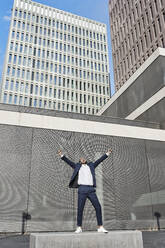 Businessman with hand raised standing in city - VEGF02666