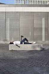 Businessman listening to music while lying in city - VEGF02670