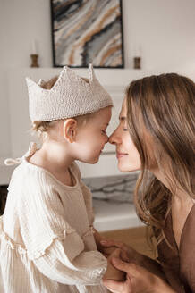 Girl in crown touches nose to nose of her mother holding hands. - CAVF88232