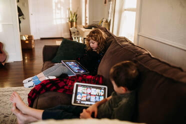 Junge Schwester und Bruder schauen Filme auf Tablets, während sie krank zu Hause sind - CAVF88235