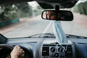 Nahaufnahme einer Gesichtsschutzmaske, die am Rückspiegel im Auto hängt - EBBF00545