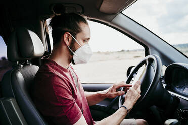 Man using smart phone while wearing protective face mask in car - EBBF00547