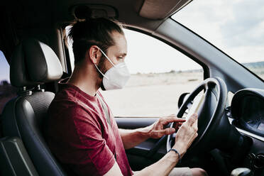 Mann benutzt Smartphone, während er im Auto eine Gesichtsschutzmaske trägt - EBBF00547