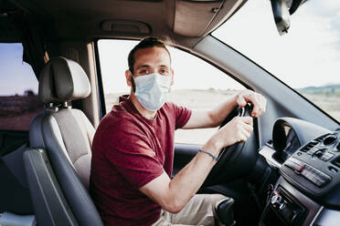 Mann mit Gesichtsmaske sitzt während COVID-19 im Auto - EBBF00550