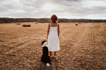 Woman standing by dog in field - EBBF00551