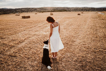 Woman standing by dog in field during sunset - EBBF00552