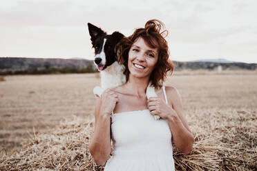 Smiling woman with dog in field during sunset - EBBF00574