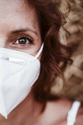 Close-up of woman wearing face mask against hay during pandemic - EBBF00576