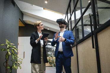 Businesswoman analyzing colleague using virtual simulation headset in creative office corridor - VPIF02662