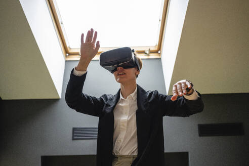 Geschäftsfrau gestikuliert, während sie ein Virtual-Reality-Simulator-Headset im Büro trägt - VPIF02682