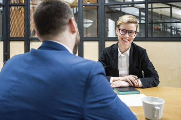 Lächelnde Geschäftsfrau, die während eines Vorstellungsgesprächs eine männliche Führungskraft im Sitzungssaal ansieht - VPIF02707