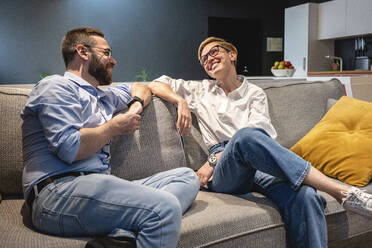 Smiling male and female professional colleagues talking while sitting on sofa in illuminated office - VPIF02713