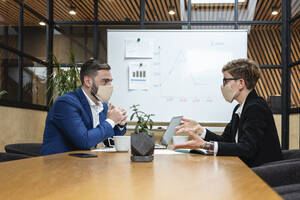 Business colleagues planning strategy while sitting at desk in board room during coronavirus pandemic - VPIF02714