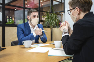 Male and female entrepreneurs wearing masks while planning strategy at desk in board room during coronavirus pandemic - VPIF02716