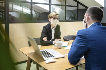 Weibliche und männliche Kollegen mit Masken bei der Strategieplanung am Schreibtisch im Sitzungssaal während einer Epidemie - VPIF02717