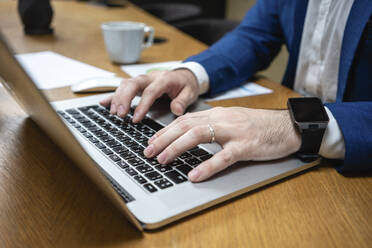 Close-up of businessman typing while using laptop at desk in creative coworking space - VPIF02721
