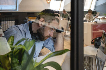 Besorgter männlicher Berufstätiger mit Blick auf den Laptop in einem kreativen Coworking-Büro - VPIF02754